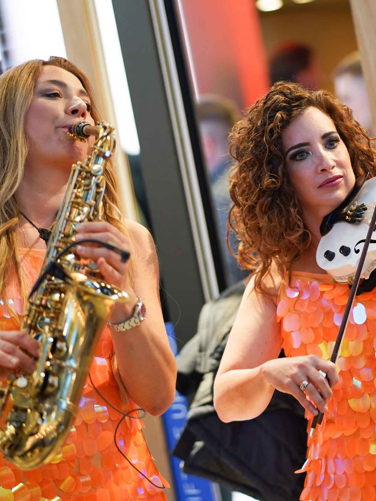 Saxophonistin und Geigerin in orangefarbenen Pailletten-Kleidern bei einer Messeparty in Köln